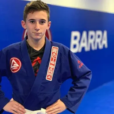Un adolescent en kimono bleu Gracie Barra, mains sur les hanches