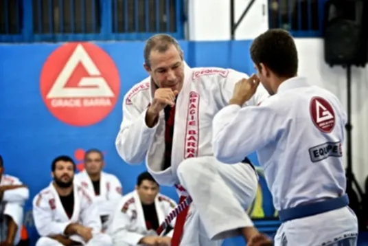 Carlos Gracie Jr. en kimono, devant le logo Gracie Barra