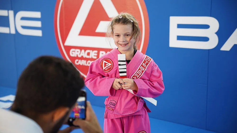 Une élève en kimono rose répond à une interview devant le logo Gracie Barra